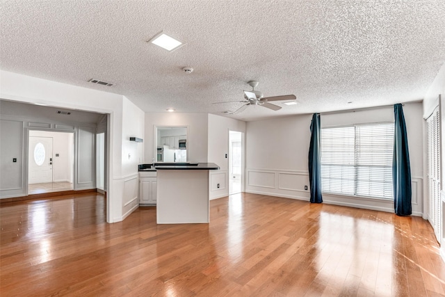 kitchen with ceiling fan, a textured ceiling, light wood finished floors, open floor plan, and dark countertops