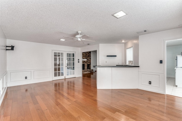 unfurnished living room featuring ceiling fan, wood finished floors, a textured ceiling, a wainscoted wall, and a fireplace