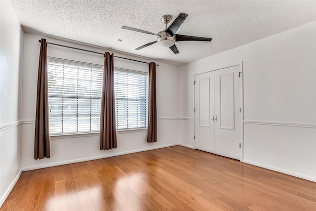 unfurnished bedroom with wood finished floors, a textured ceiling, baseboards, a closet, and ceiling fan