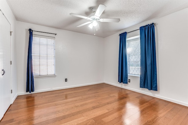 unfurnished room featuring light wood finished floors, healthy amount of natural light, a ceiling fan, a textured ceiling, and baseboards