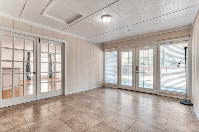 tiled spare room featuring french doors, healthy amount of natural light, wooden walls, and baseboards