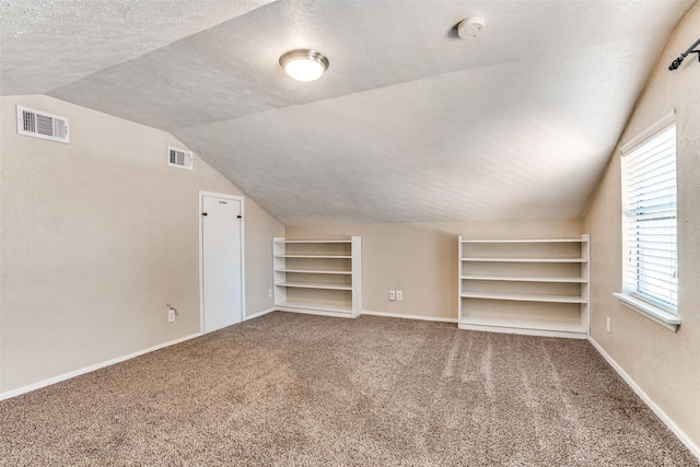 additional living space featuring vaulted ceiling, carpet flooring, built in shelves, baseboards, and a textured ceiling
