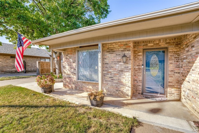 view of exterior entry featuring brick siding and fence