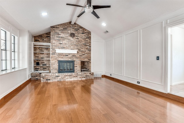 unfurnished living room featuring a ceiling fan, light wood-style flooring, a decorative wall, a fireplace, and built in shelves