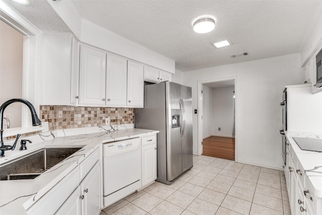 kitchen featuring white dishwasher, a sink, stainless steel refrigerator with ice dispenser, white cabinetry, and a textured ceiling