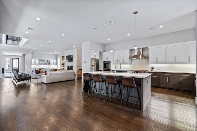 kitchen featuring wall chimney exhaust hood, stainless steel appliances, a sink, light countertops, and a kitchen breakfast bar