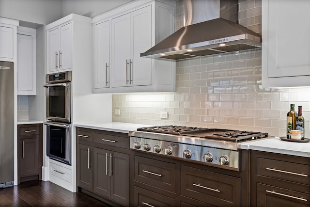 kitchen featuring wall chimney range hood, appliances with stainless steel finishes, light countertops, and backsplash