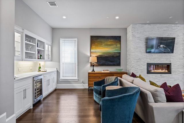 living room with wine cooler, dark wood finished floors, a dry bar, baseboards, and a stone fireplace