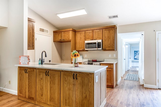 4626 Nervin St, The Colony, TX 75056 - kitchen featuring a sink, stainless steel appliances, brown cabinetry, light wood-type flooring, and a peninsula