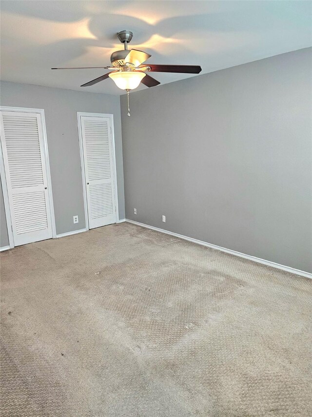 unfurnished bedroom featuring two closets, carpet flooring, baseboards, and ceiling fan
