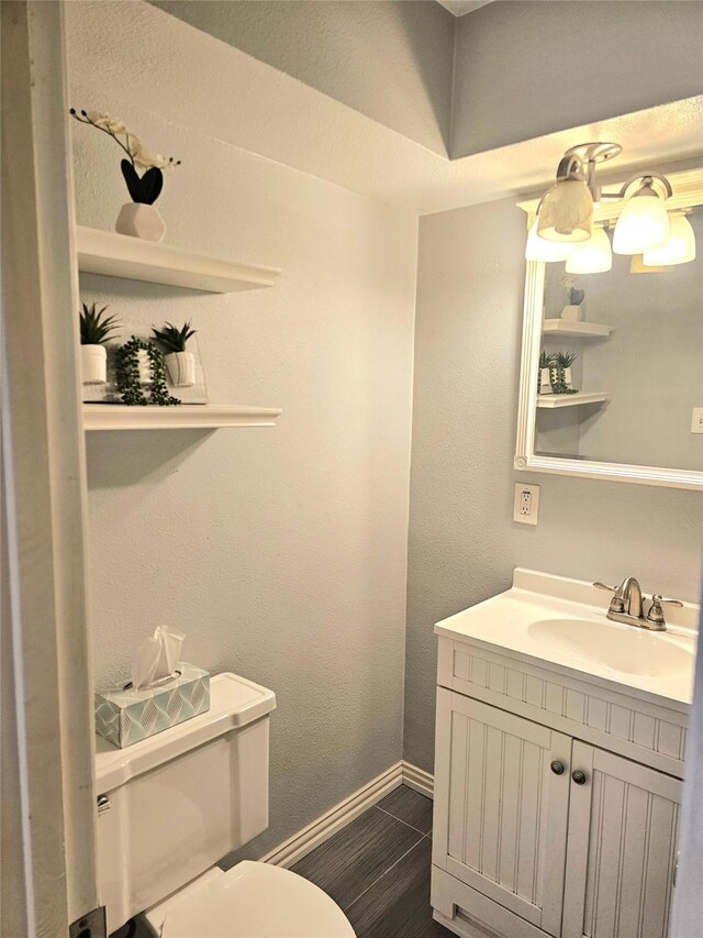 half bathroom with toilet, vanity, baseboards, and wood finished floors