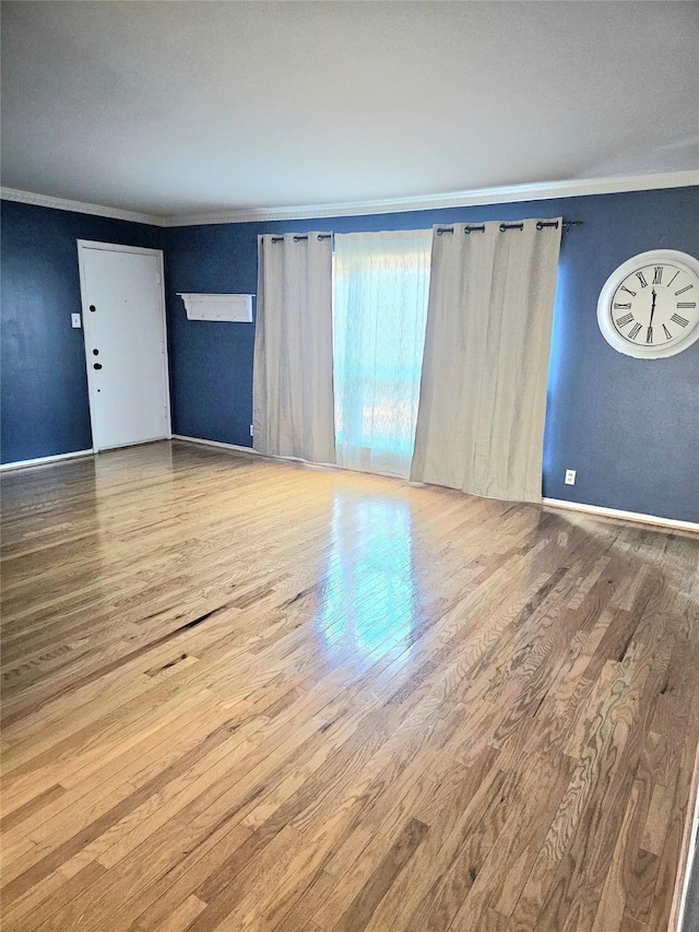unfurnished living room featuring wood finished floors, crown molding, and baseboards