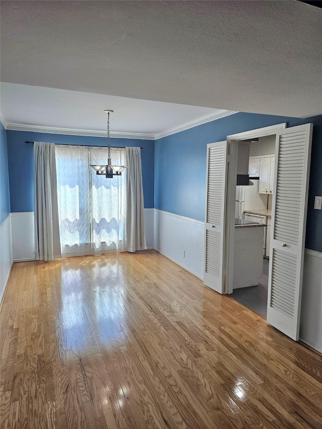 unfurnished dining area with a wainscoted wall, a chandelier, hardwood / wood-style flooring, ornamental molding, and a textured ceiling