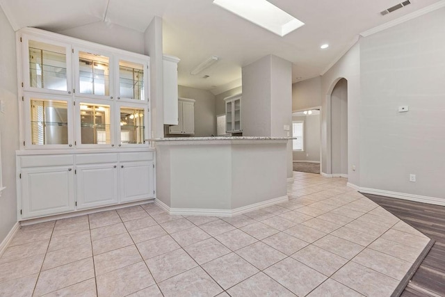 1501 Milla Ct, Euless, TX 76039 - kitchen featuring light tile patterned floors, white cabinetry, a skylight, baseboards, and arched walkways