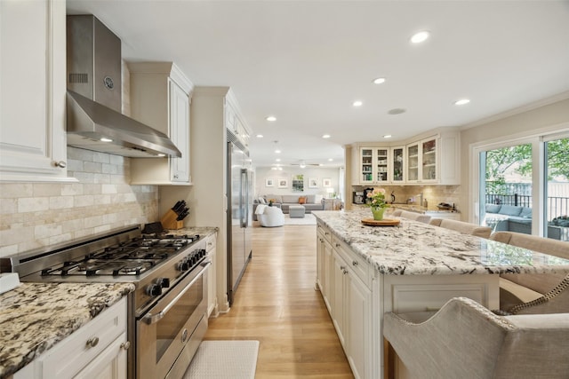 7008 Joyce Way, Dallas, TX 75225 - kitchen featuring stainless steel appliances, wall chimney exhaust hood, open floor plan, a center island, and light wood finished floors