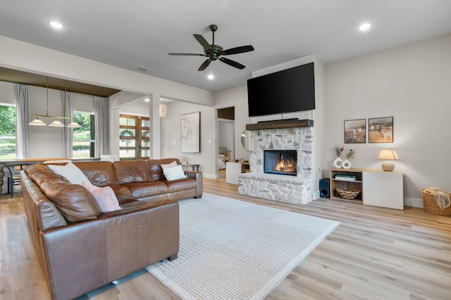 living area with a stone fireplace, a ceiling fan, light wood-type flooring, baseboards, and recessed lighting