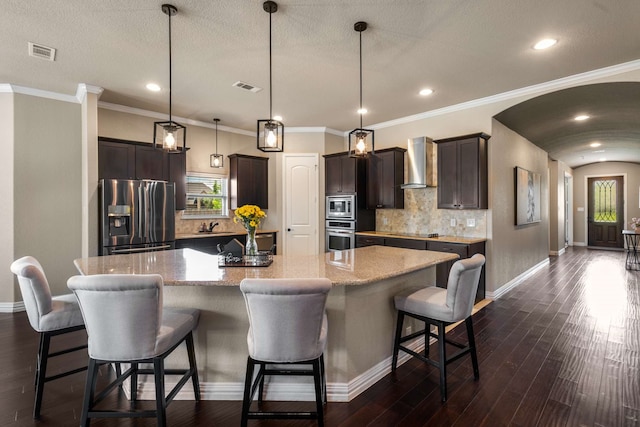958 Prairie Timber Rd, Burleson, TX 76028 - kitchen with appliances with stainless steel finishes, wall chimney range hood, dark brown cabinets, backsplash, and a large island with sink