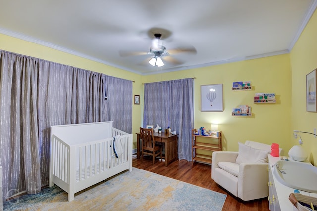 bedroom with crown molding, a crib, wood finished floors, and a ceiling fan