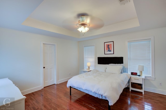 bedroom featuring a raised ceiling, baseboards, wood finished floors, and a ceiling fan