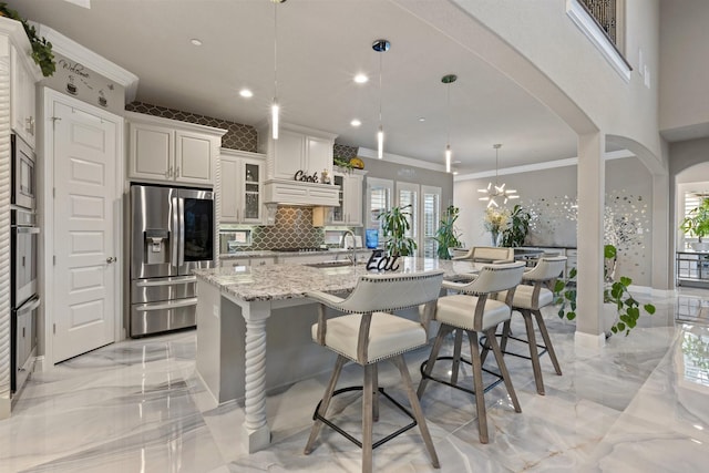 2604 Coyote Xing, Rockwall, TX 75087 - kitchen with appliances with stainless steel finishes, light marble finish floors, arched walkways, a breakfast bar, and ornamental molding