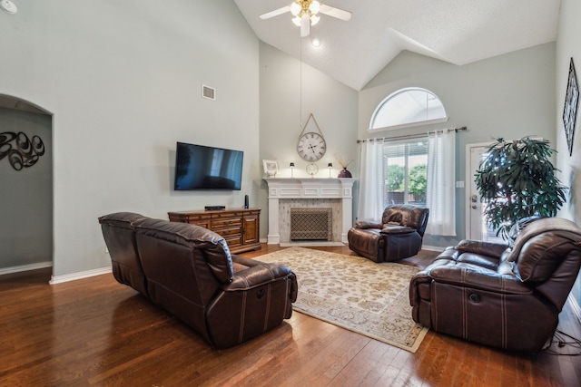living area with a ceiling fan, hardwood / wood-style floors, high vaulted ceiling, a fireplace with flush hearth, and baseboards