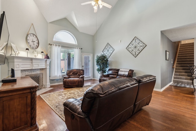 living room featuring wood finished floors, a premium fireplace, stairway, ceiling fan, and high vaulted ceiling