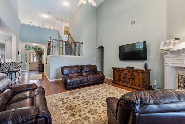 living room featuring a towering ceiling, ceiling fan, wood finished floors, baseboards, and a fireplace