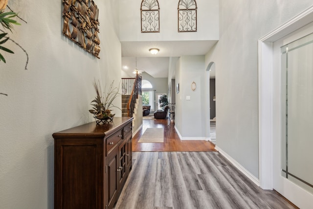 foyer with arched walkways, wood finished floors, baseboards, and a high ceiling