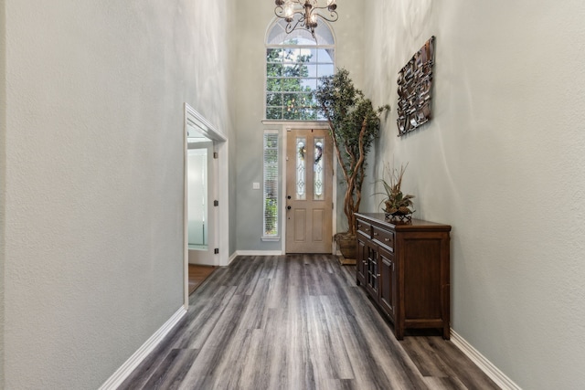 foyer featuring baseboards, dark wood-type flooring, a chandelier, a high ceiling, and a textured wall