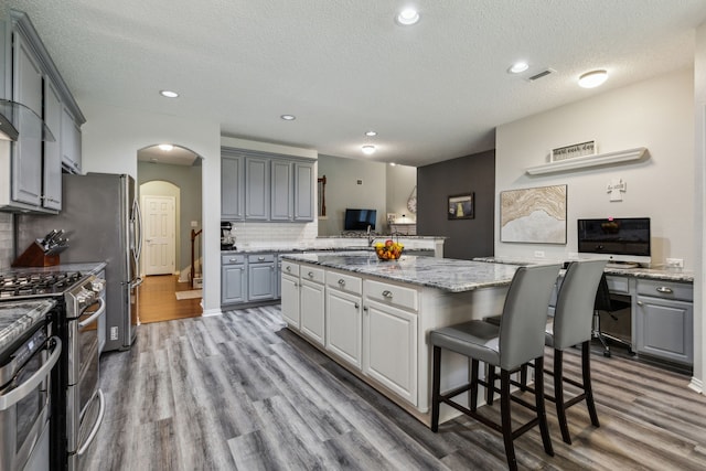 kitchen with range with two ovens, arched walkways, wood finished floors, a kitchen island, and gray cabinetry