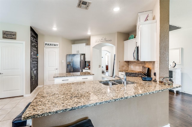 820 Lake Sierra Way, Little Elm, TX 75068 - kitchen featuring appliances with stainless steel finishes, a sink, light stone counters, a peninsula, and arched walkways