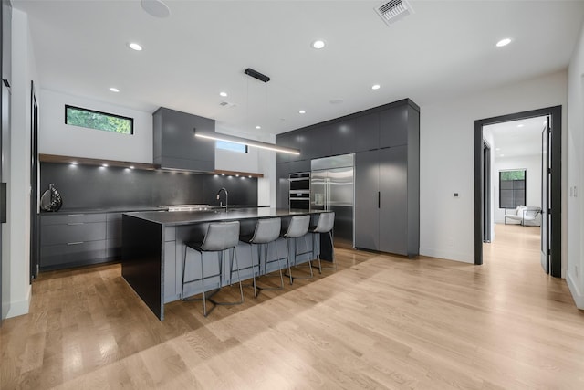 10026 Mccree Rd, Dallas, TX 75238 - kitchen with modern cabinets, stainless steel appliances, dark countertops, a kitchen bar, and light wood-style floors