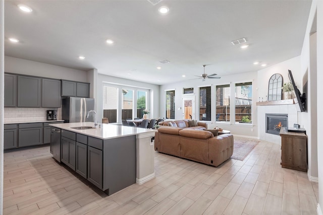 1106 Sassafras Dr, Princeton, TX 75407 - kitchen featuring gray cabinets, stainless steel appliances, light countertops, a tiled fireplace, and tasteful backsplash