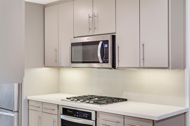 kitchen with stainless steel appliances, backsplash, gray cabinets, and light countertops