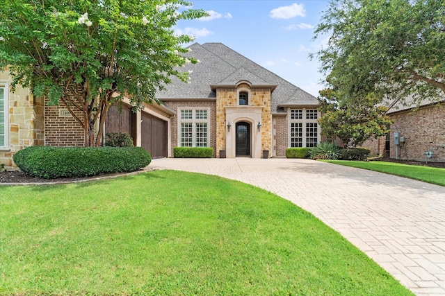 french country style house with driveway, an attached garage, stone siding, a front lawn, and brick siding