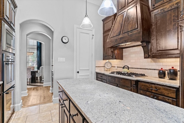 kitchen featuring appliances with stainless steel finishes, arched walkways, tasteful backsplash, baseboards, and light stone countertops