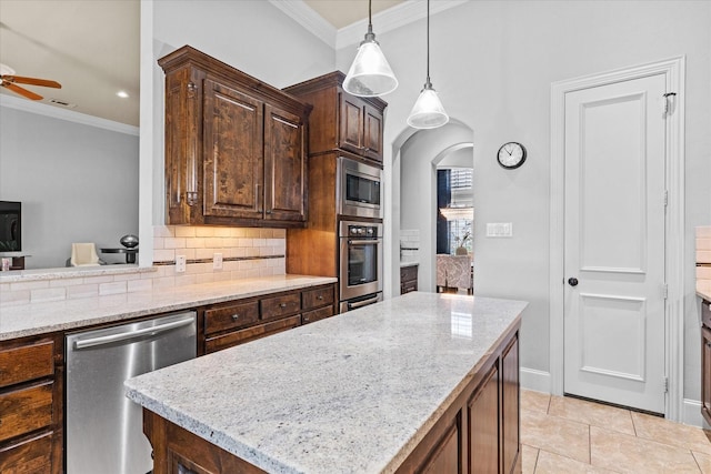 kitchen featuring appliances with stainless steel finishes, ornamental molding, decorative backsplash, light stone counters, and a ceiling fan