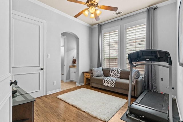 workout room featuring arched walkways, ceiling fan, light wood-style flooring, ornamental molding, and baseboards