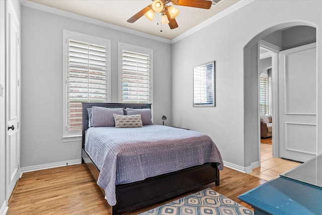 bedroom featuring arched walkways, light wood-style floors, baseboards, ornamental molding, and a ceiling fan