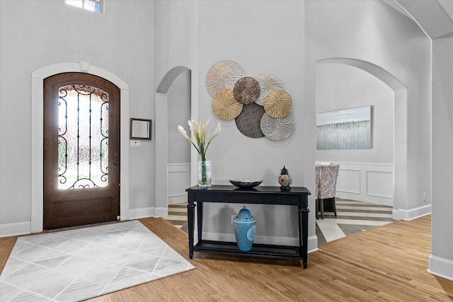 foyer with arched walkways, a high ceiling, light wood finished floors, and baseboards