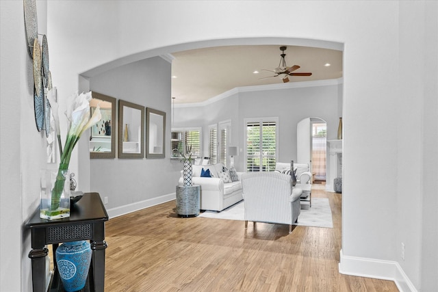 living room featuring ceiling fan, arched walkways, crown molding, wood finished floors, and baseboards