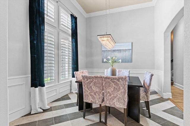 tiled dining room featuring crown molding, a chandelier, a wainscoted wall, and a decorative wall