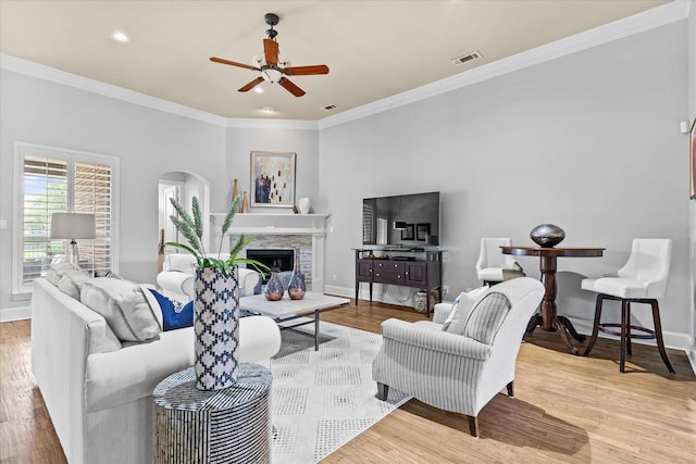 living area with arched walkways, a ceiling fan, baseboards, ornamental molding, and wood finished floors