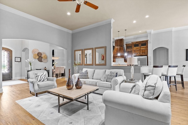 living room featuring arched walkways, a ceiling fan, ornamental molding, recessed lighting, and light wood-style floors