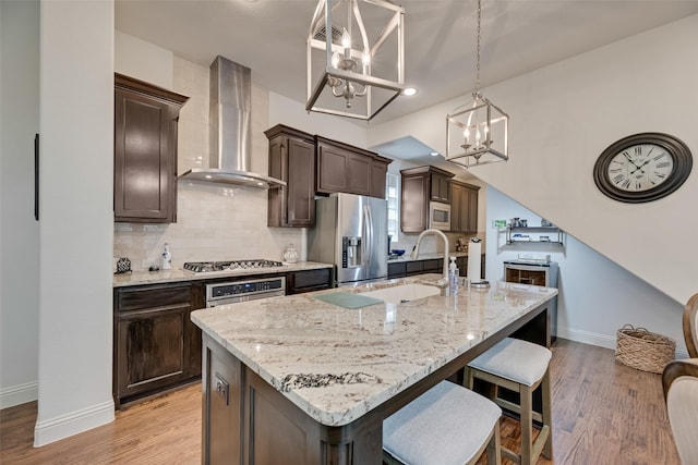 7320 San Saba Dr, Mckinney, TX 75070 - kitchen featuring wall chimney exhaust hood, appliances with stainless steel finishes, a chandelier, dark brown cabinets, and decorative backsplash