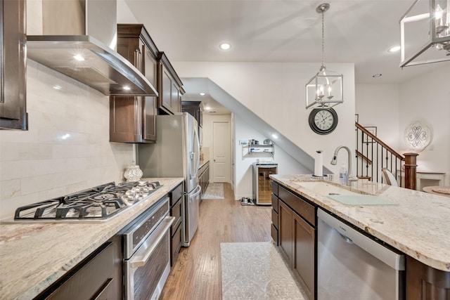 7320 San Saba Dr, Mckinney, TX 75070 - kitchen with appliances with stainless steel finishes, wall chimney exhaust hood, dark brown cabinetry, hanging light fixtures, and backsplash