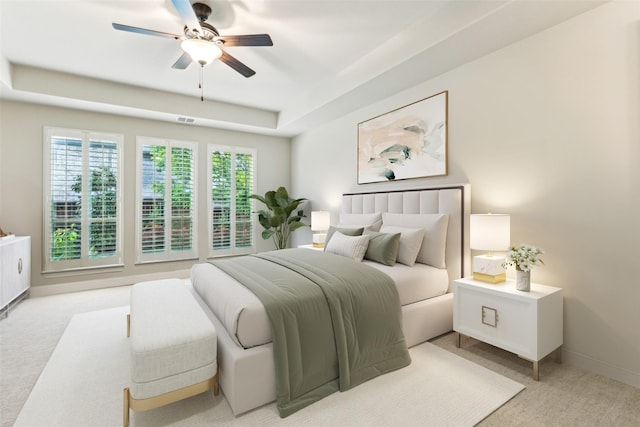 bedroom featuring light colored carpet, a raised ceiling, baseboards, and a ceiling fan