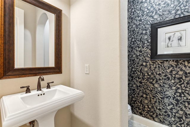 bathroom featuring a sink, wallpapered walls, and toilet