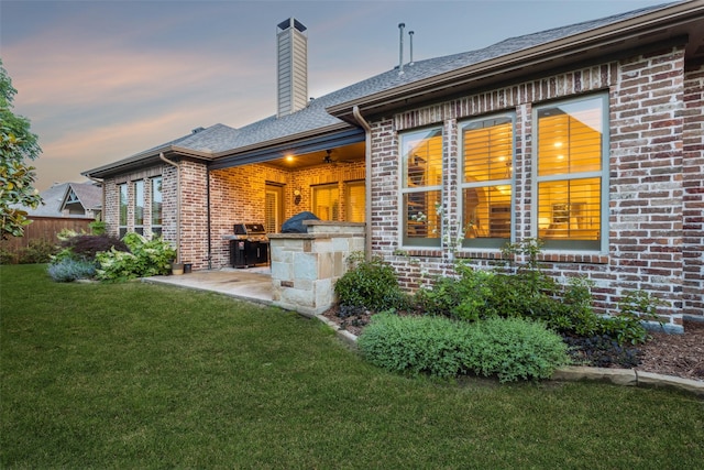 back of house at dusk with brick siding, a patio, a ceiling fan, a chimney, and exterior kitchen