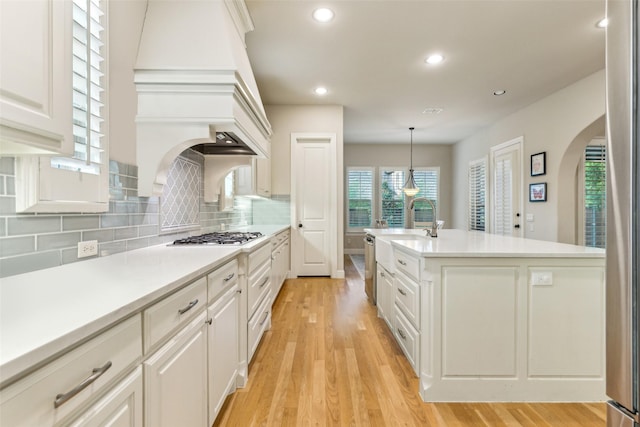 kitchen with arched walkways, stainless steel gas stovetop, a sink, light wood-style floors, and backsplash